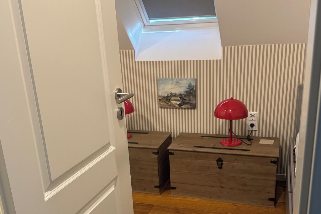 A room with a wooden desk, two red lamps, a painting on the wall, and a skylight above.