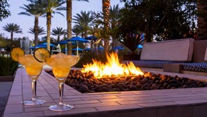 Two cocktails on a patio with a fire feature and palm trees in the background.