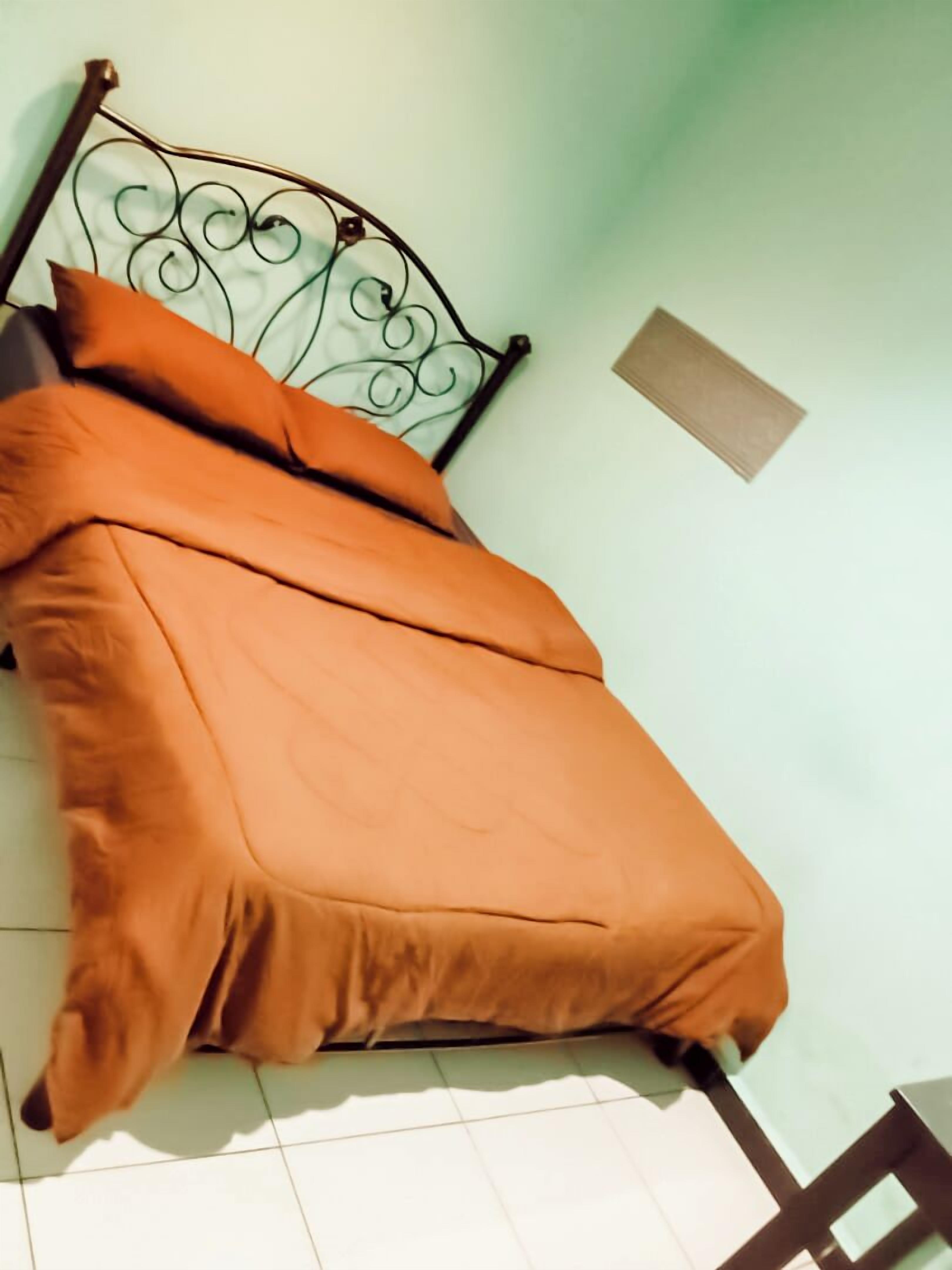 A bed with an orange bedspread and pillows, a metal headboard, and a small window on the wall.