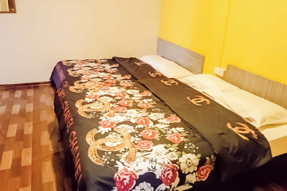 Ein Bett mit Blumenmuster auf der Bettwäsche und einem Kopfteil vor einer gelben Wand.
