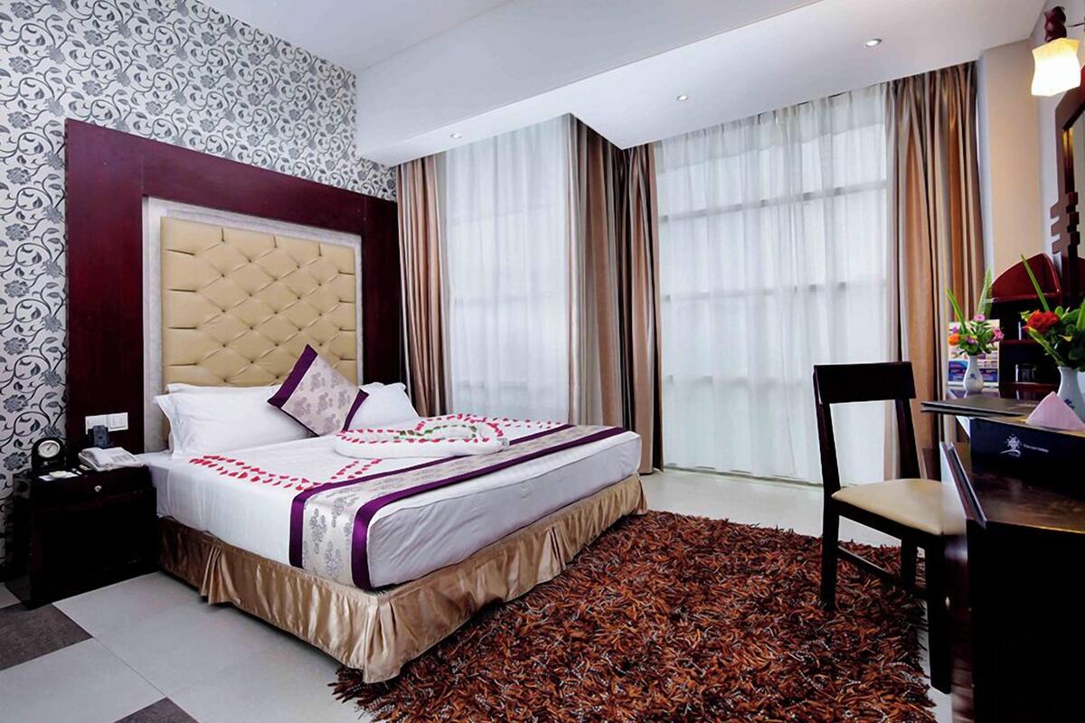 A hotel room with a large bed, a desk with a chair, and a window with curtains.