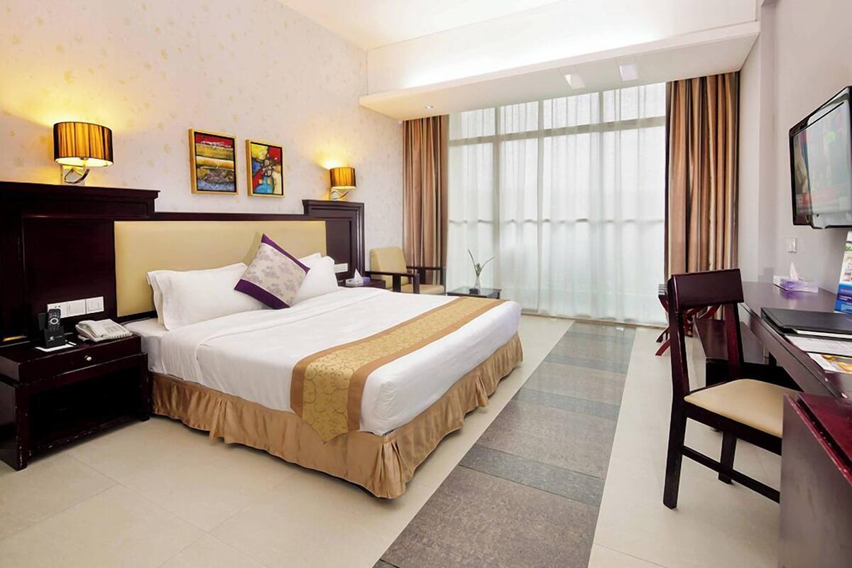 A hotel room with a large bed, a desk, a chair, and a TV.