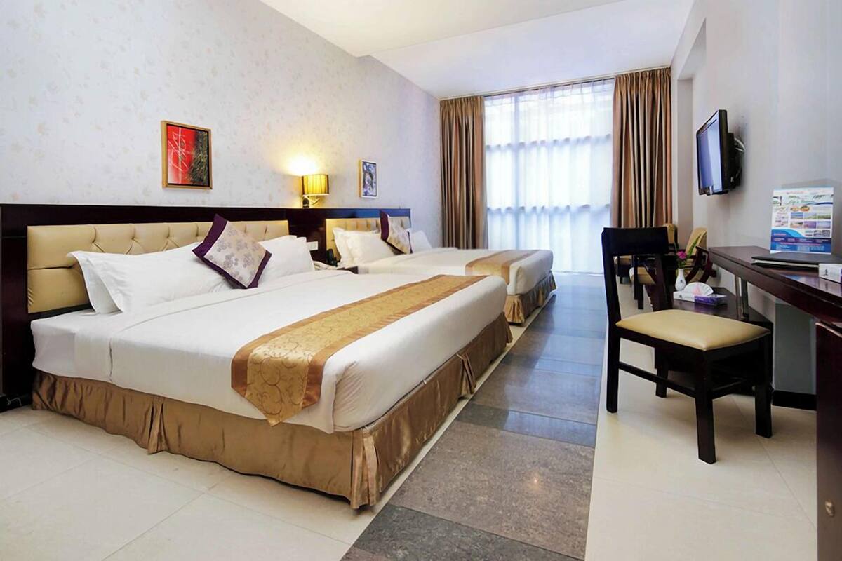 A hotel room with two beds, a desk, a chair, a TV, and a window with curtains.