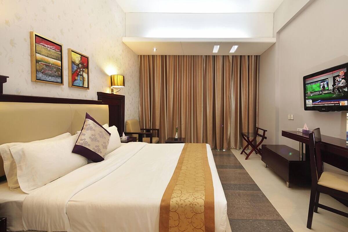 A hotel room with a large bed, a desk, a chair, a television, and a curtain.