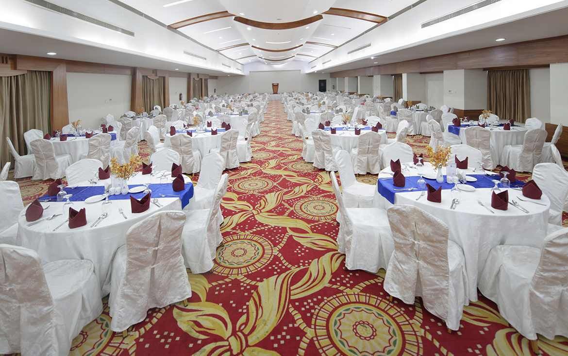 A banquet hall with round tables, white chairs, and a red carpet.