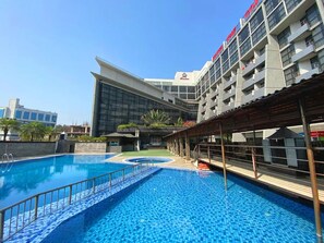 Ein Pool mit gefliestem Deck, einem überdachten Sitzbereich und einem modernen Gebäude mit Balkonen im Hintergrund.