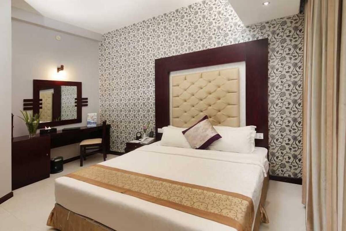 A hotel room with a large bed, a bedside table, a mirror, and patterned wallpaper.