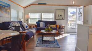 A cozy living room with a sofa, a coffee table, and a dining table. There is a sign above the door that reads "CAPE COD." - Completely renovated 3 bedroom cottage, .2 miles from Glendon Road beach (Dennis Port)