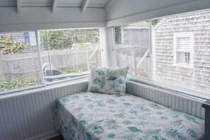 Cozy bedroom with a single bed and marine-themed quilt, featuring large windows with white blinds.