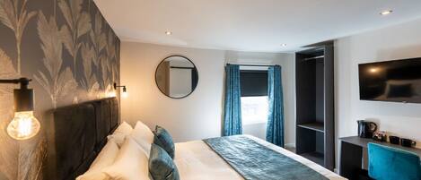 A modern hotel room with a large bed, a desk, a TV, and a wardrobe.