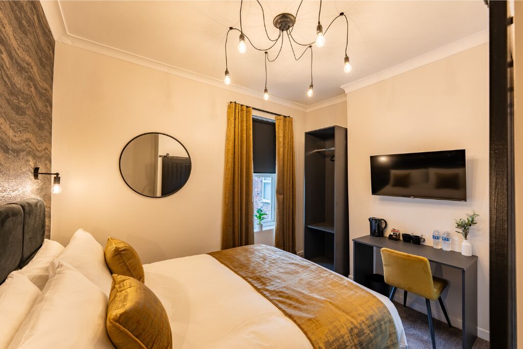 A hotel room with a bed, a desk, a television, and a mirror.