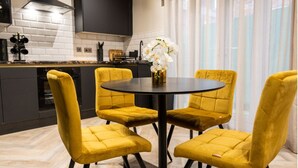 A modern kitchen with a black countertop, white brick backsplash, and a black range hood. There is a round table with four yellow chairs and a vase with white flowers. - Home at 42 Arkles Lane (Liverpool)
