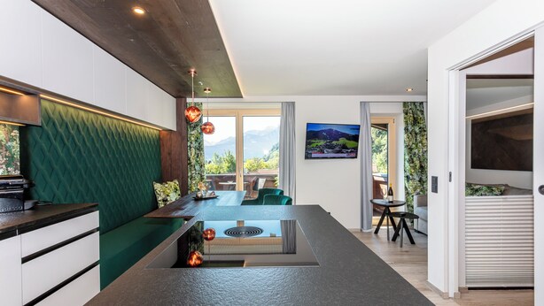 Una cocina moderna con una isla central, un comedor con vistas y un espacio de sala con sofá y televisor.