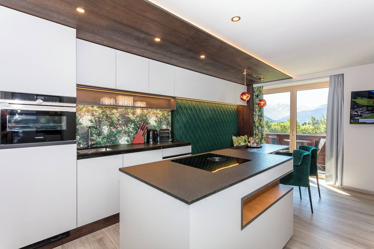 Una cocina moderna con armarios blancos, una isla integrada y vistas a montañas a través de amplios ventanales.
