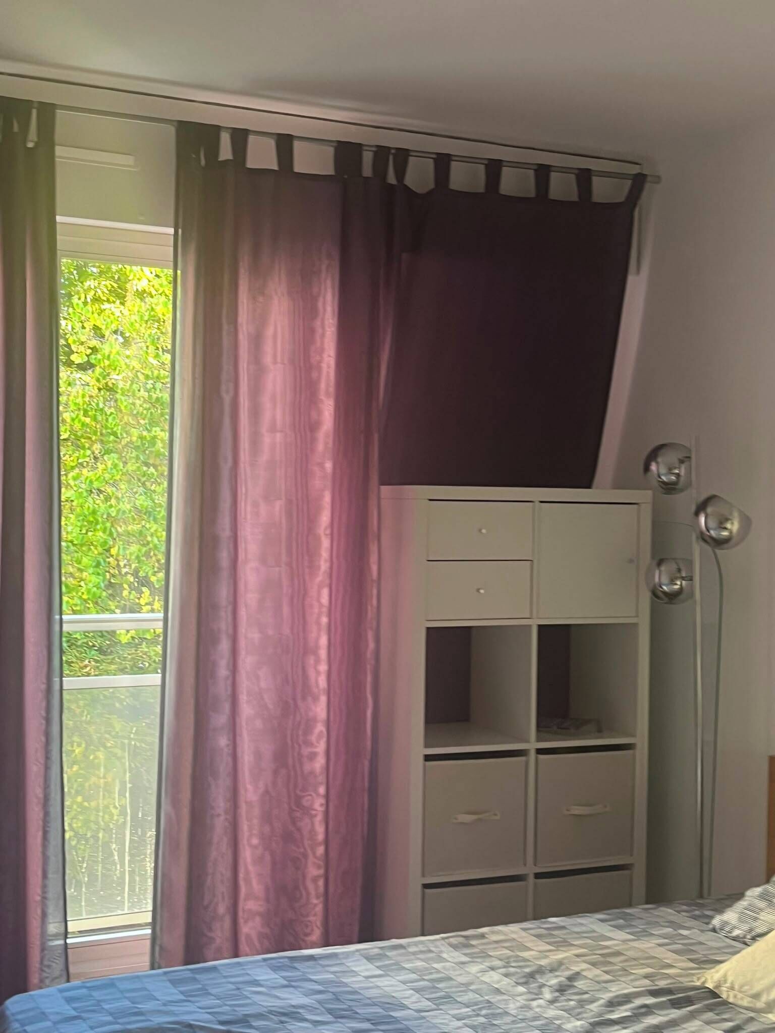 A bedroom with a bed, a wardrobe, and a window with curtains.