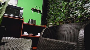 A room with a green wall, a microwave, a small shelf with glasses, and a wicker chair. - Sunzal Bungalows (Tamanique)