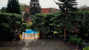 Un jardin à l’arrière de la maison, avec une piscine, entouré d’arbres touffus et d’une clôture en bois.