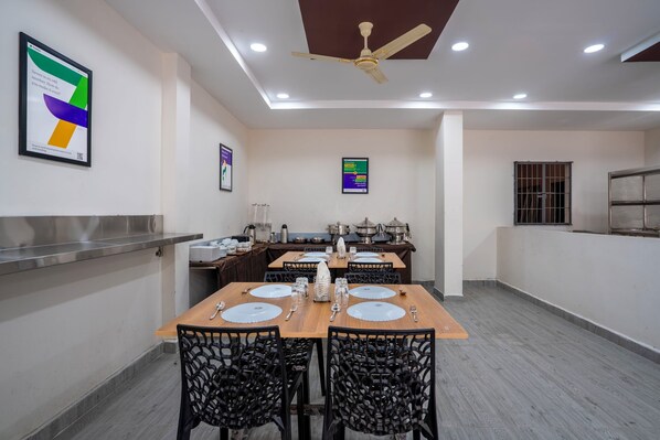 A dining area with tables set for four, chairs, a ceiling fan, and a kitchen area in the background. - Treebo The Living Tree Karimnagar (Karimnagar)