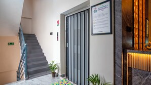 Eine Hotelhalle mit einer Marmortreppe, einem gerahmten Nachhaltigkeitsleitfaden, einem Feuerschutzschild und einer Rezeption mit Marmorplatte.