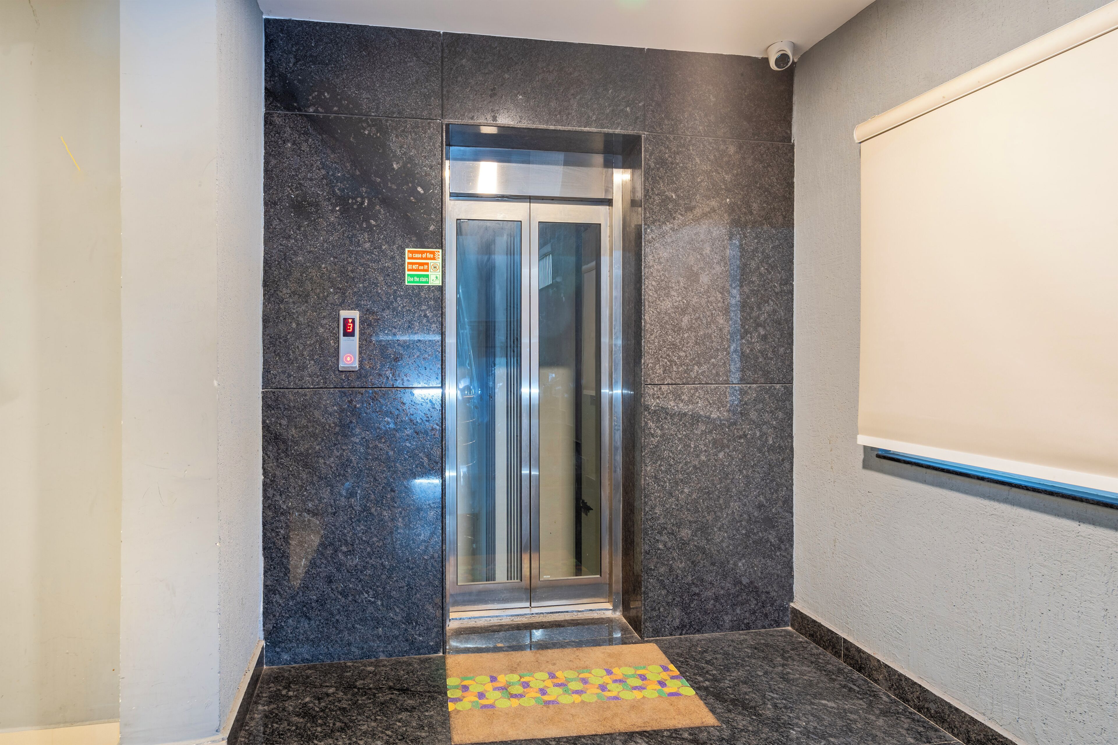 Un ascensor en un pasillo con suelo de baldosas y un letrero en la pared.