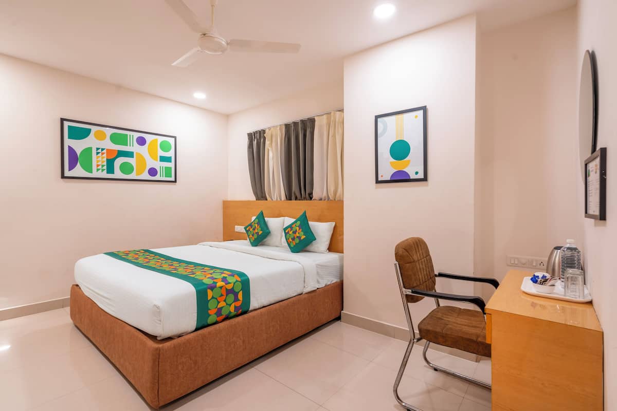 A hotel room with a bed, a desk, a chair, a ceiling fan, and artwork on the walls.