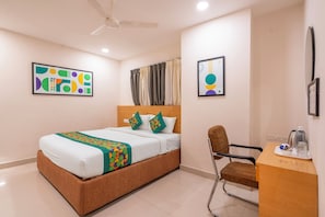 A hotel room with a bed, a desk, a chair, a ceiling fan, and artwork on the walls. - Treebo Living Tree opposite Khairatabad Metro (Hyderabad)