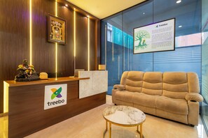 A reception area with a wooden reception desk, a sofa, a small table, and a framed picture on the wall. - Treebo Living Tree opposite Khairatabad Metro (Hyderabad)