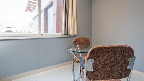 A room with a glass table and two chairs, a window with curtains, and a view of buildings outside. - Treebo Living Tree opposite Khairatabad Metro (Hyderabad)