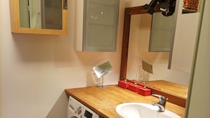 A compact bathroom with a washing machine, a sink, and a mirror.