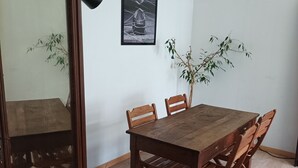 A dining area with a wooden table and chairs, a framed picture on the wall, and a potted plant.