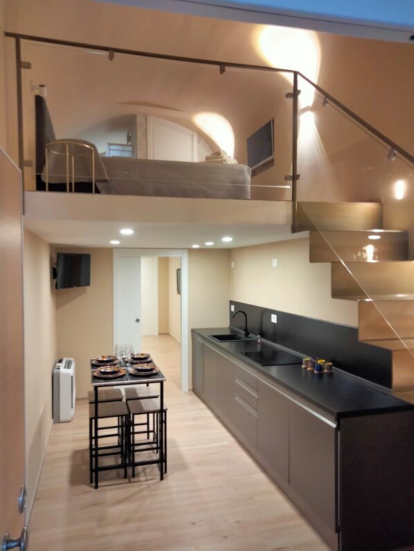 A modern kitchen with a central island, a dining area with a table set for four, and a staircase connecting two levels. - BLESSED ELIA LOFT (Bari)