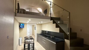 Eine moderne Küche mit einer zentralen Kochinsel, einem Essbereich mit Tisch und Stühlen sowie einer Treppe, die in einen oberen Bereich führt.