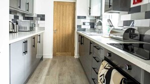 A modern kitchen with grey cabinets, a wooden door, and a stainless steel range hood. - COSY CRUISE CRIBS - MODERN HOME FROM HOME - CENTRAL LOCATION. (Stoke-on-Trent)