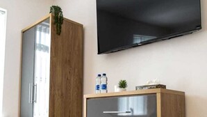 A room with a wooden wardrobe, a grey dresser with drawers, a flat-screen TV mounted on the wall, and a small plant on the dresser. - COSY CRUISE CRIBS - MODERN HOME FROM HOME - CENTRAL LOCATION. (Stoke-on-Trent)