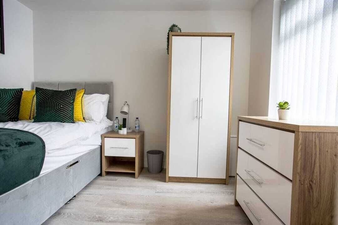 Ein Schlafzimmer mit Bett, Nachttisch, Lampe, Kleiderschrank und einer kleinen Pflanze.
