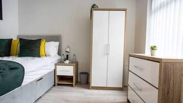 Ein Schlafzimmer mit Bett, Nachttisch, Lampe, Kleiderschrank und einer kleinen Pflanze.