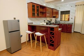 Een keuken met houten kastjes, een marmeren spatwand en een roestvrijstalen koelkast. Twee barstoelen en een klein eiland met een spoelbak.