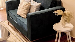 A living room with a dark green sofa, a small white side table with a decorative plant, and a framed artwork on the wall. - Sand Grains Residences 008 (Entebbe)