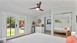 A bedroom with a large bed, a ceiling fan, a TV, and a sliding glass door leading to a balcony.