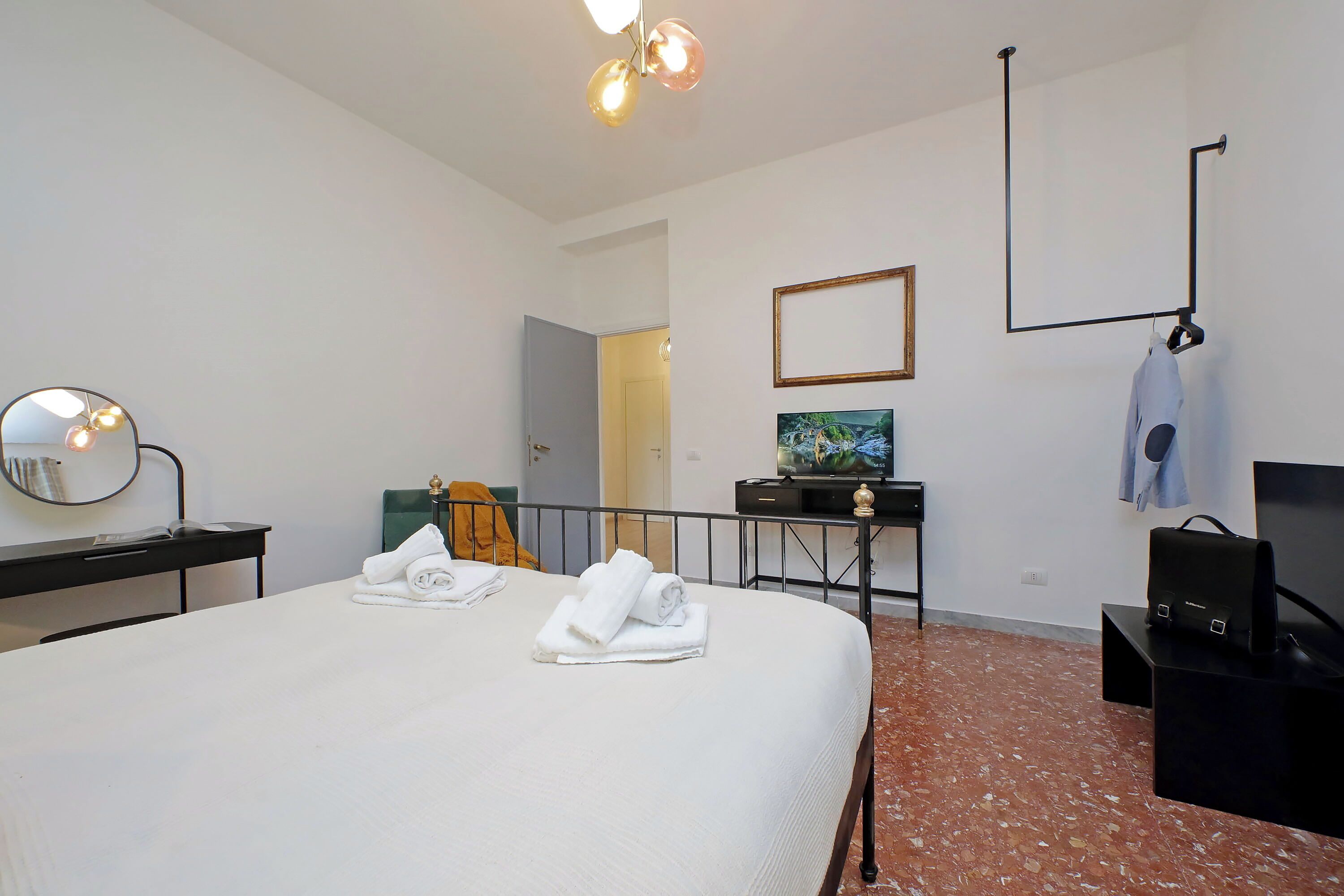 A hotel room with a large bed, a desk with a mirror, a television, and a coat rack.