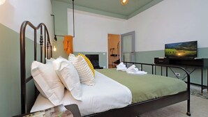 A neatly made bed with white and yellow pillows, a green bedspread, and a television on a stand to the right. - TM Apartment (Rome)