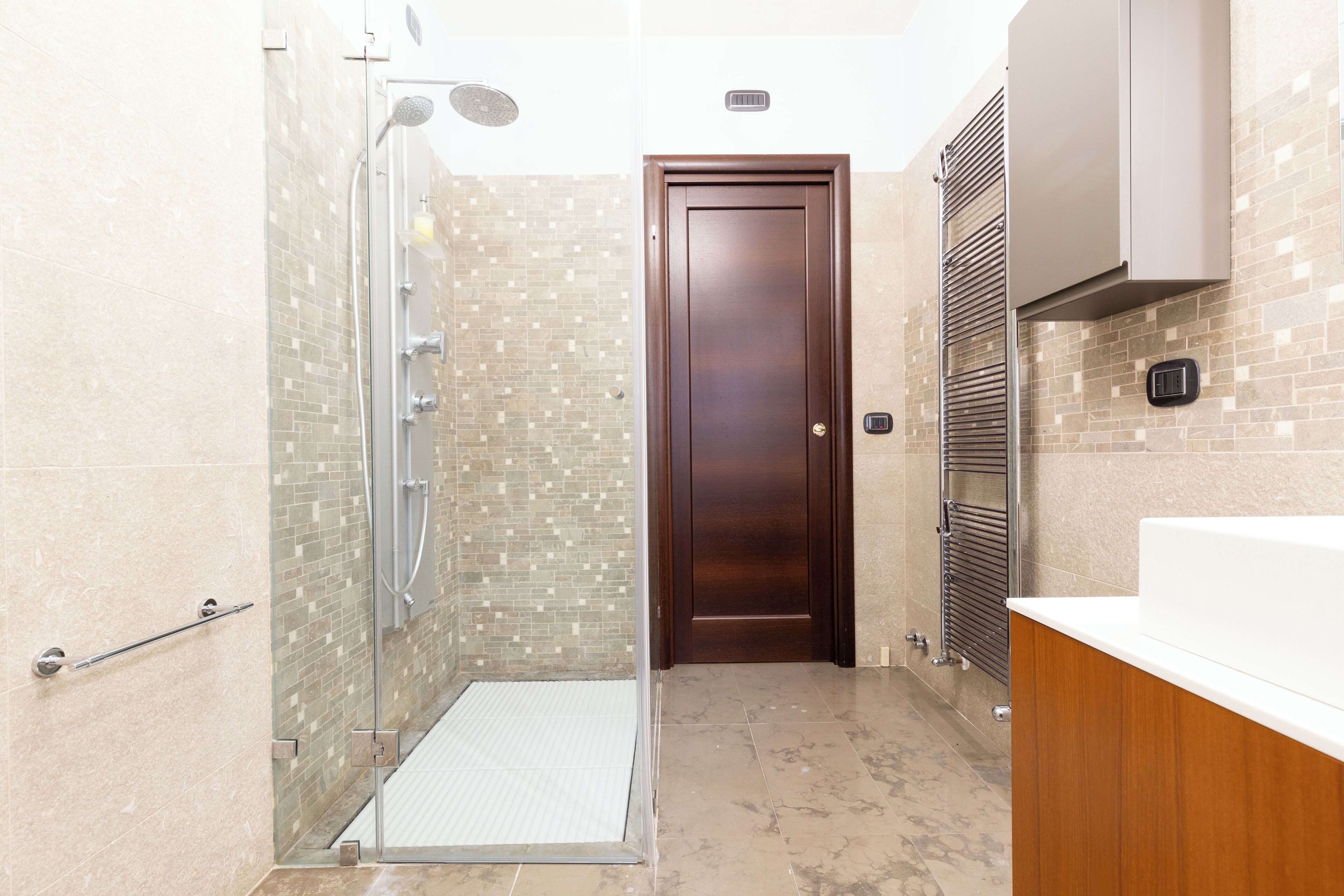 A modern bathroom with a glass shower enclosure, a wooden door, and a white sink.