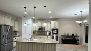 A modern kitchen with a central island, stainless steel appliances, pendant lighting, and a black cart. - Spacious 5-bedroom house in peaceful Midway with WiFi, AC Close to Savannah GA  (Midway)