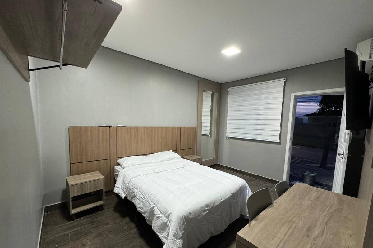 A modern bedroom with a bed, bedside tables, a wooden desk, and a window with blinds.