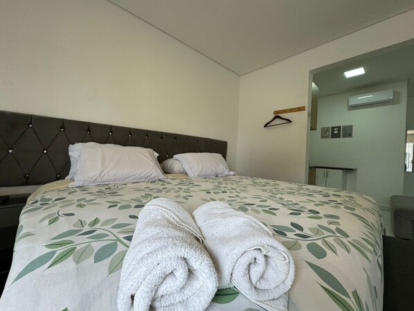 A neatly made bed with a leaf-patterned bedspread, two rolled towels, and a hanging coat rack. - John R Hotel Curitiba (Curitiba)