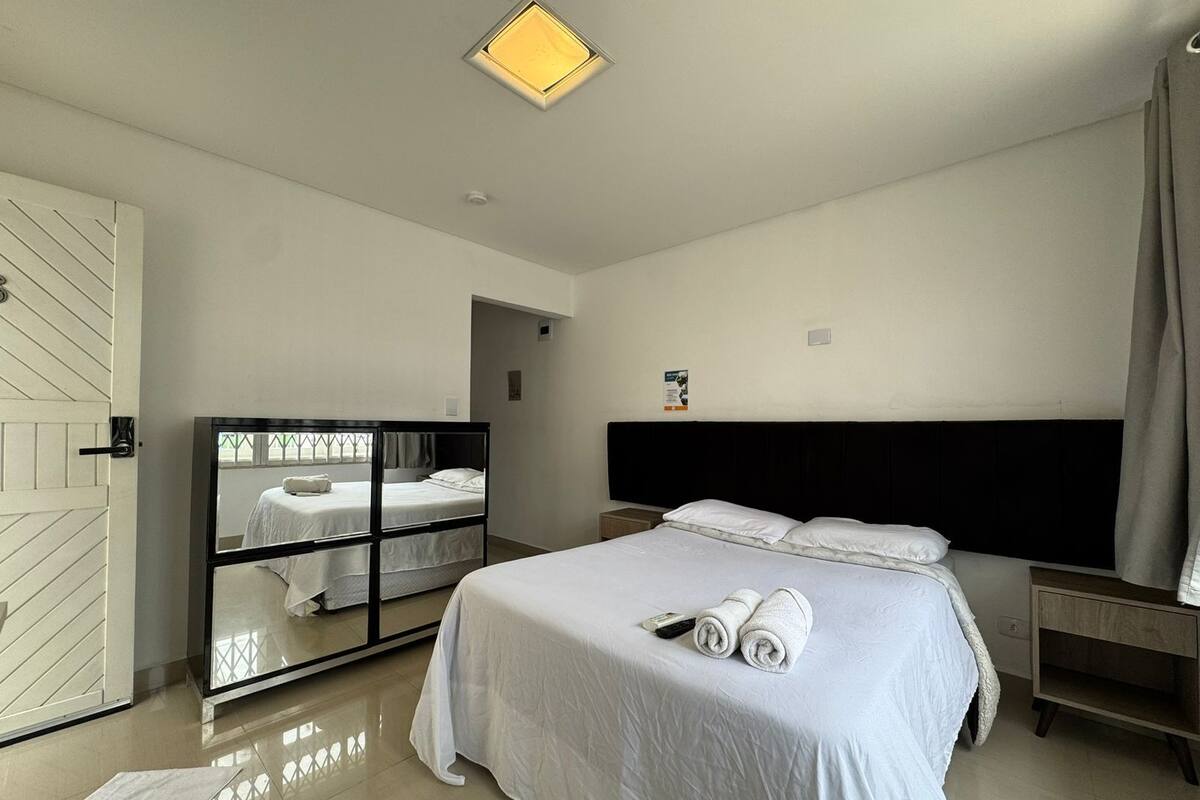 A modern hotel room with a large bed, a mirror, a bedside table, and a door with a unique design.