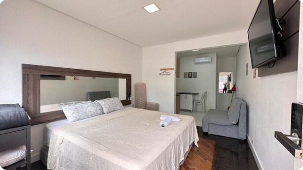 Una camera d'albergo con un letto grande, una TV a parete, un divano grigio e una scrivania piccola con una sedia.