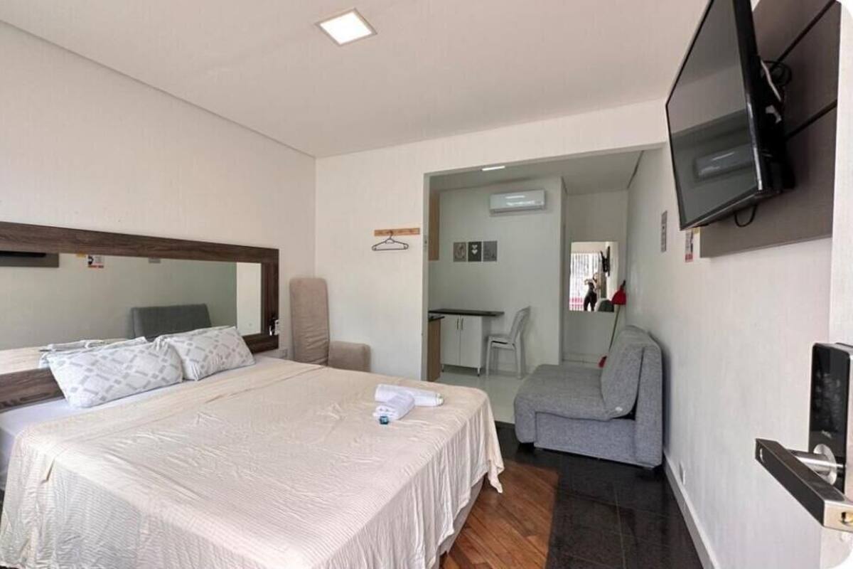 A hotel room with a large bed, a TV mounted on the wall, a grey sofa, and a small desk with a chair.