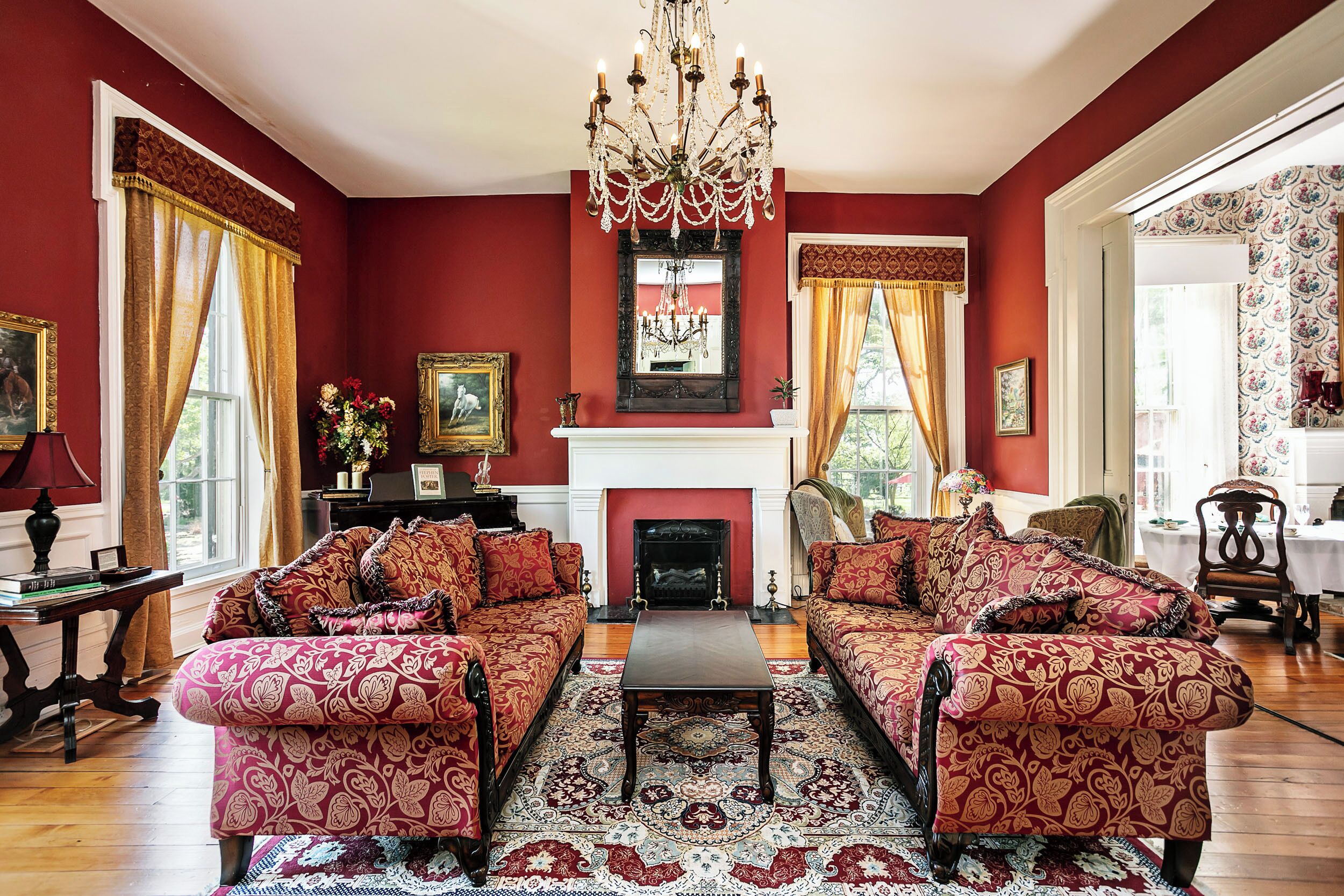 A traditional living room with a fireplace, red walls, and patterned furniture.