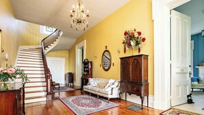 A spacious living room with hardwood floors, a staircase, a chandelier, a sofa, a cabinet, and a floral arrangement. - 7 Private Rooms, Country Setting Bourbon Trail, patio/firepit. Breakfast inc. (Springfield)